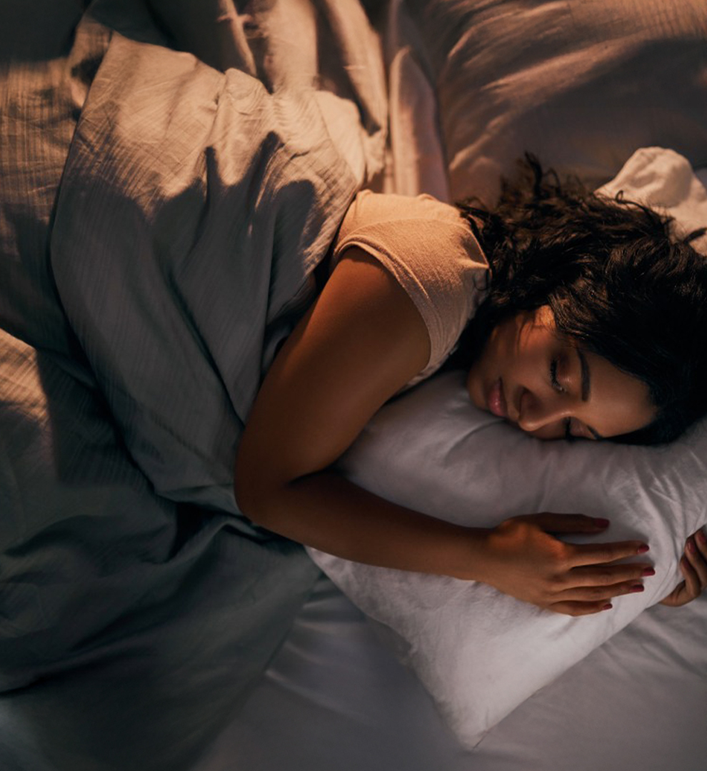 Woman sleeping on a bed holding a pillow in a dim room.
