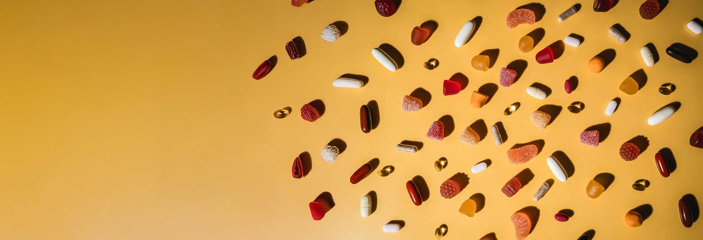 Gummies, tablets, and softgel supplements laid out on a yellow background.
