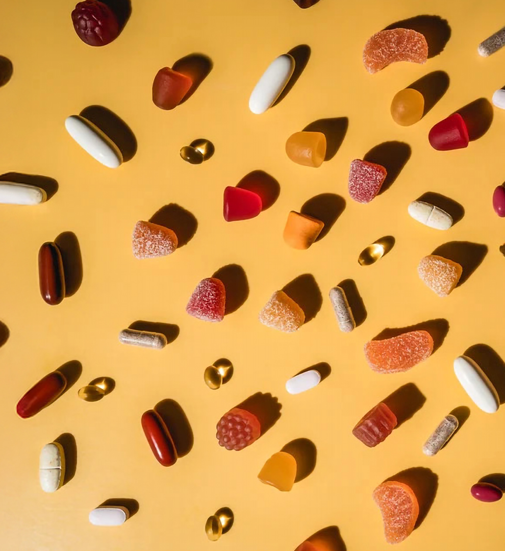 Gummies, tablets, and softgel supplements laid out on a yellow background.