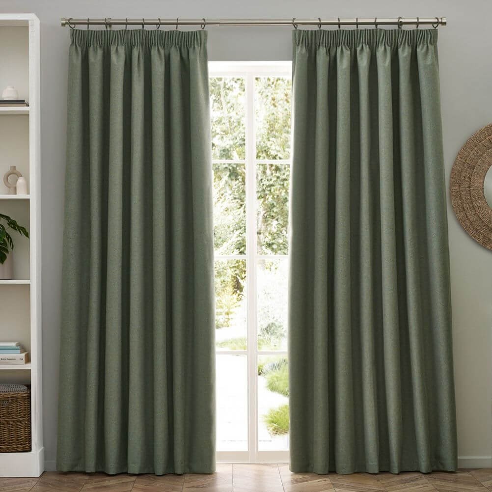 Blackout pencil pleat curtains in a eucalyptus green shade hung on a metal curtain pole.