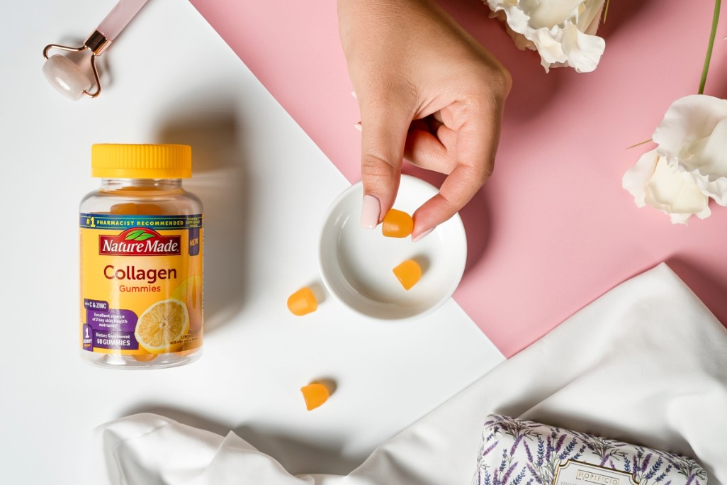 Nature Made Collagen Gummies bottle with gummies and hand on a pink and white surface