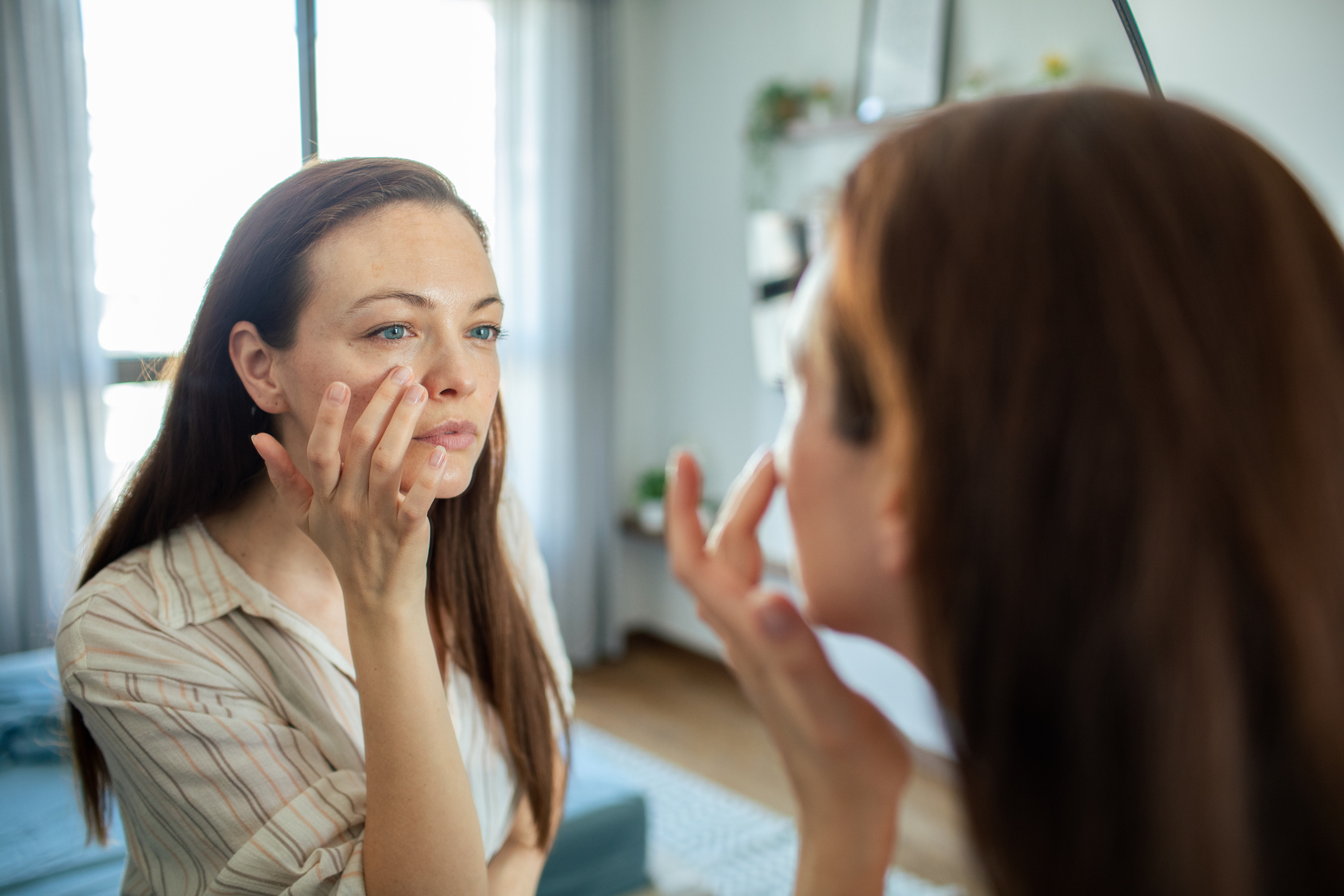 Person touching face while looking in a mirror at home