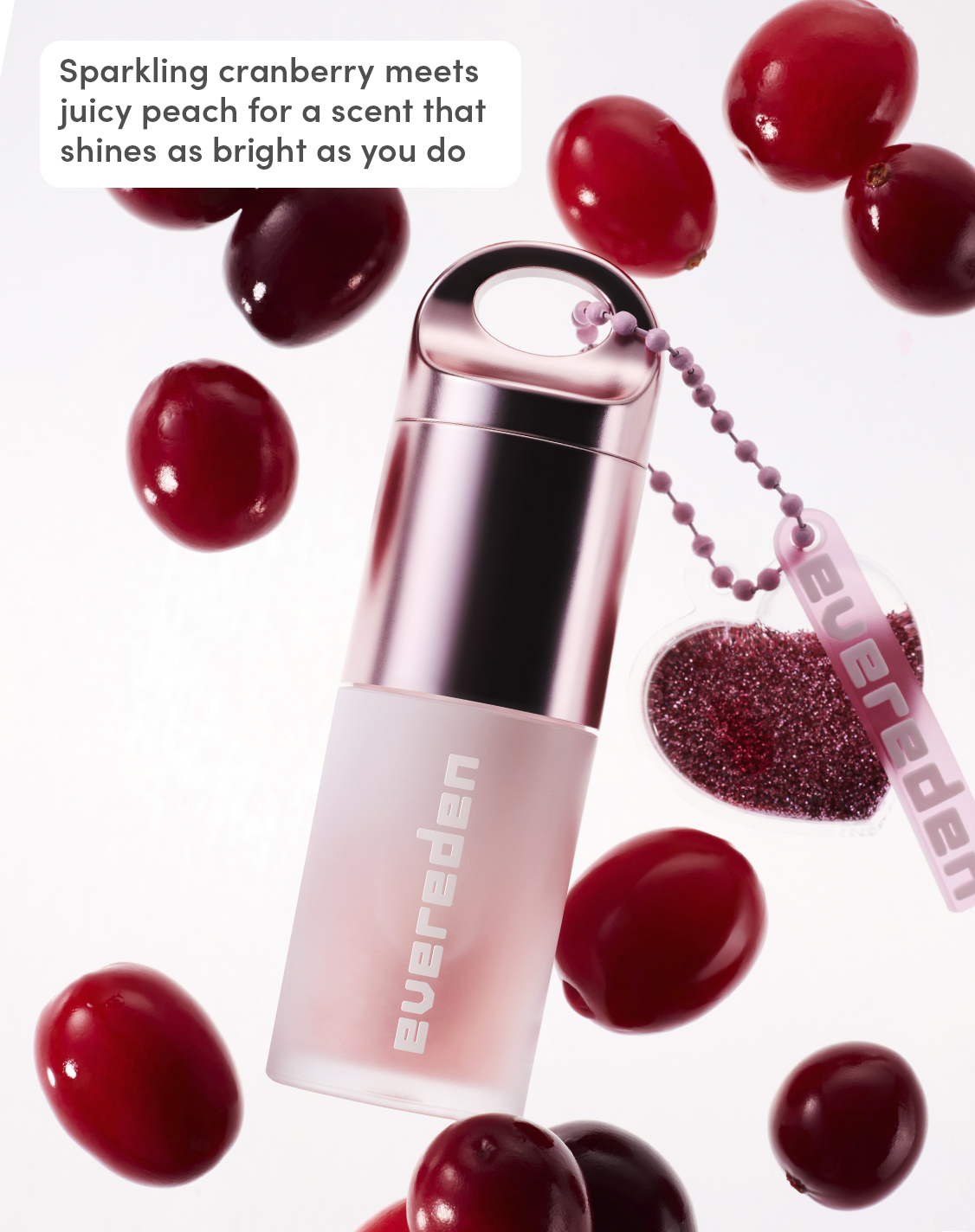 Evereden Pink Stardust Hydrating Tinted Lip Oil with heart charm surrounded by cranberries, highlighting its sparkling cranberry and juicy peach scent.