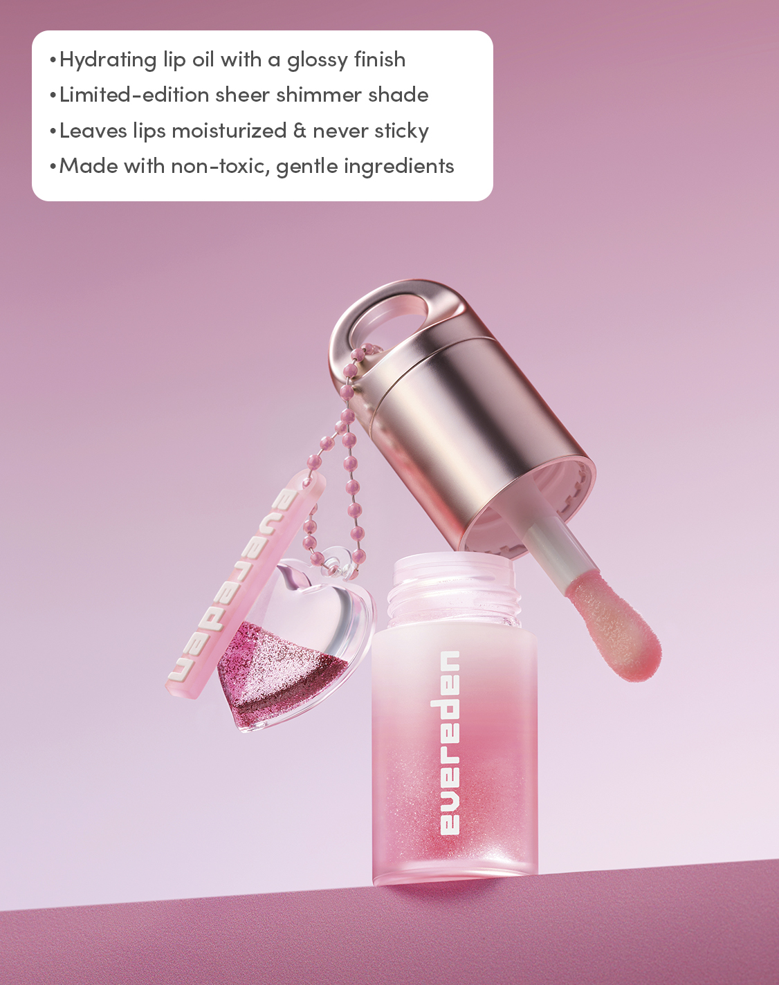 Open Evereden Pink Stardust Hydrating Tinted Lip Oil with applicator and glitter heart charm, highlighting its hydrating, non-sticky, sheer shimmer formula made with gentle, non-toxic ingredients.