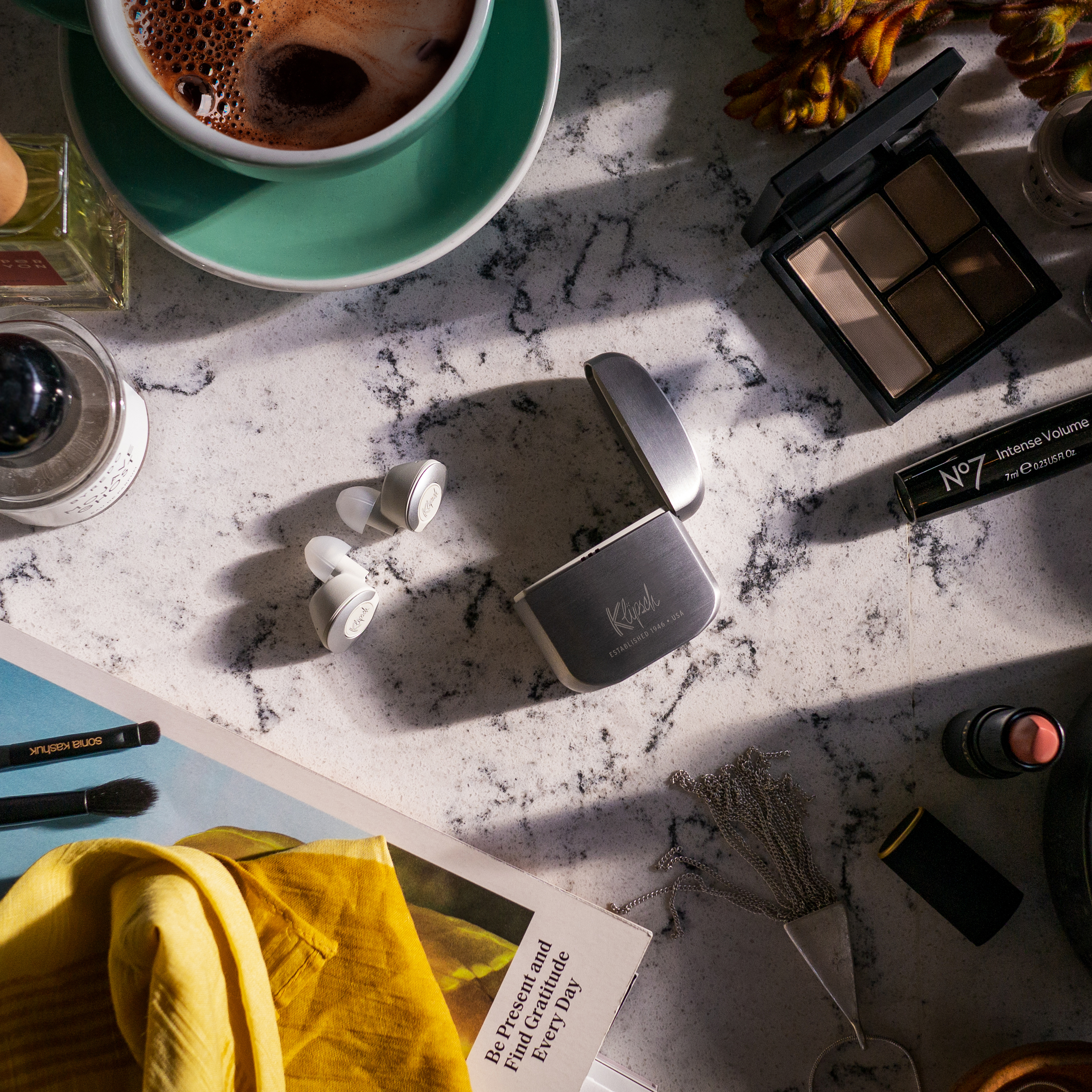 Flatlay of Klipsch T5 II True Wireless earbuds, coffee and some makeup on a marble table