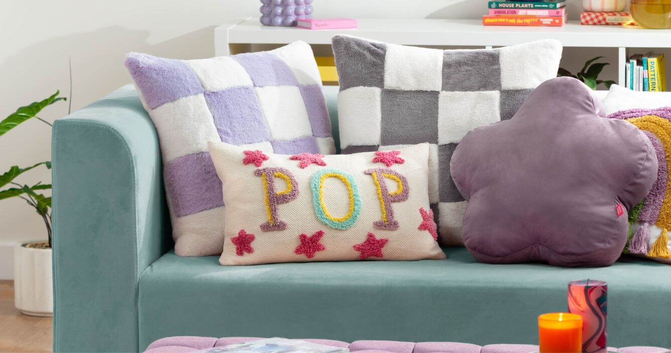 A selection of brightly-coloured scatter cushions with check and embroidered designs, displayed on a blue sofa in a living room.