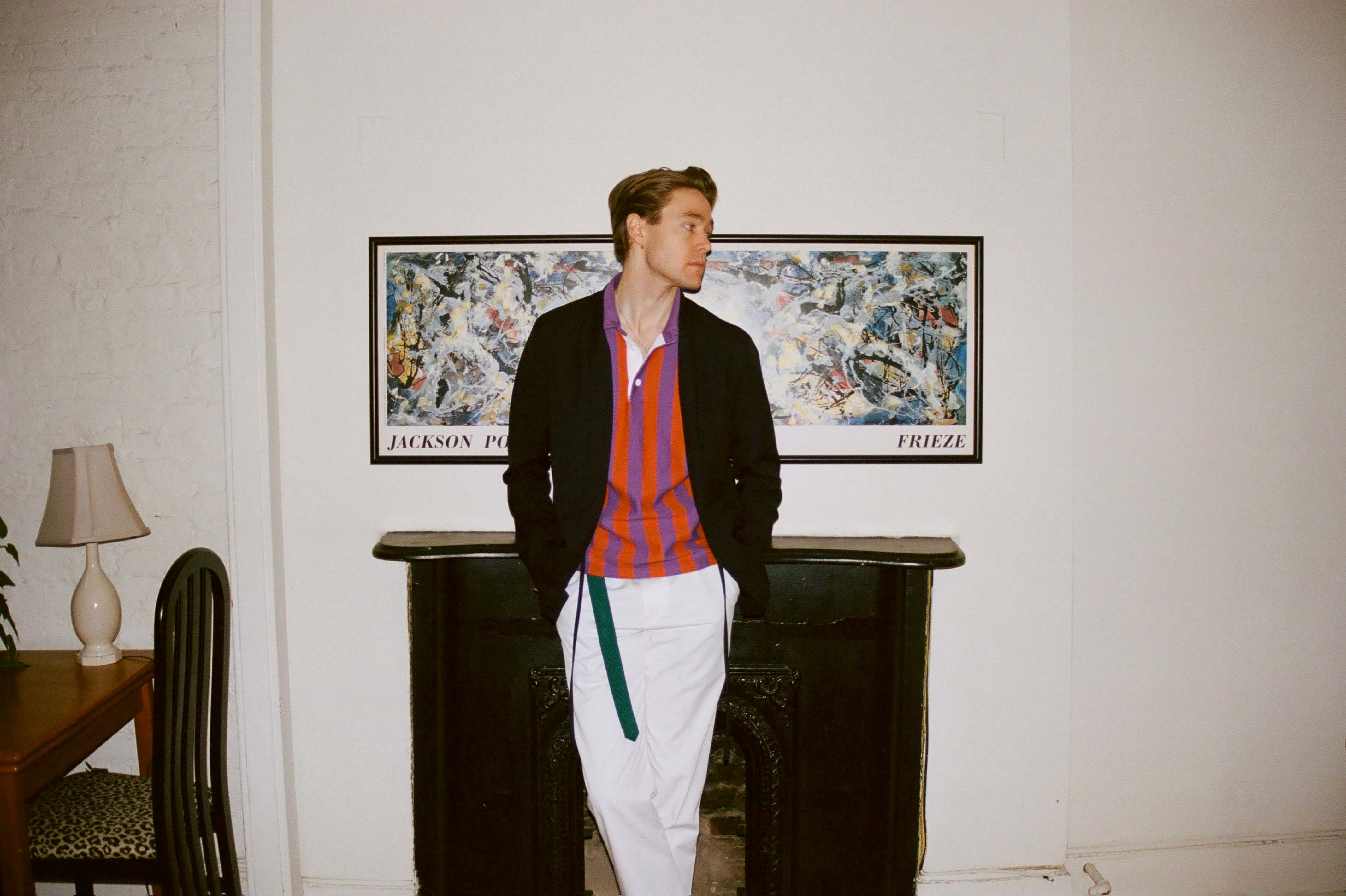 Male model wearing the Cream Twill Wide Leg Trousers, the Game Rugby in orange and purple and the Latin Boat Strap  Belt in green