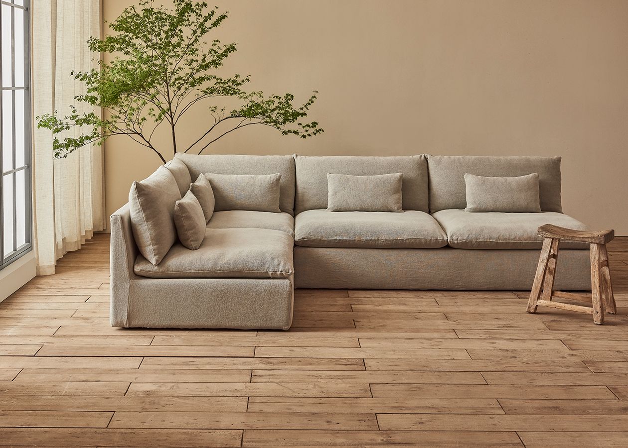 Aria L Shape Sectional in Medium Weight Linen Jasmine Rice, placed in a sunlit room next to a window