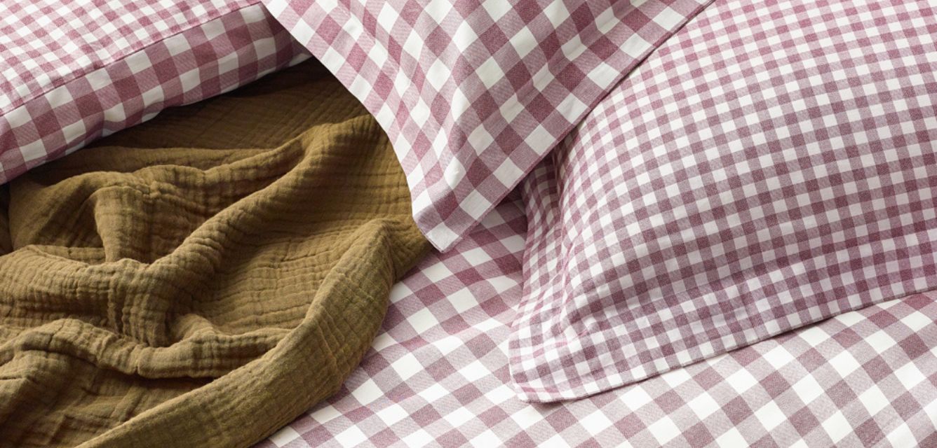 Burgundy and white checkered bedding set with a khaki green textured blanket draped on top. 
