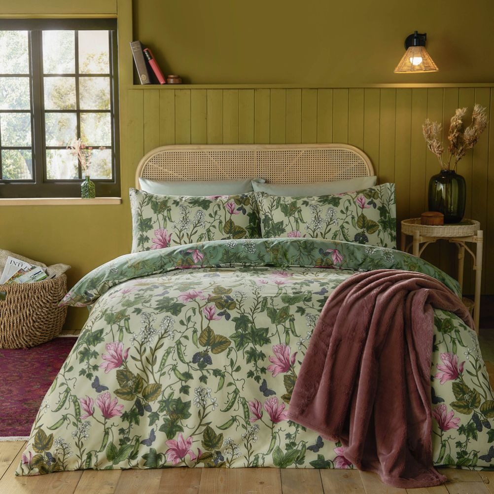 A cosy bedroom featuring a floral duvet, pink flowers, and green accents on a wooden bed. 