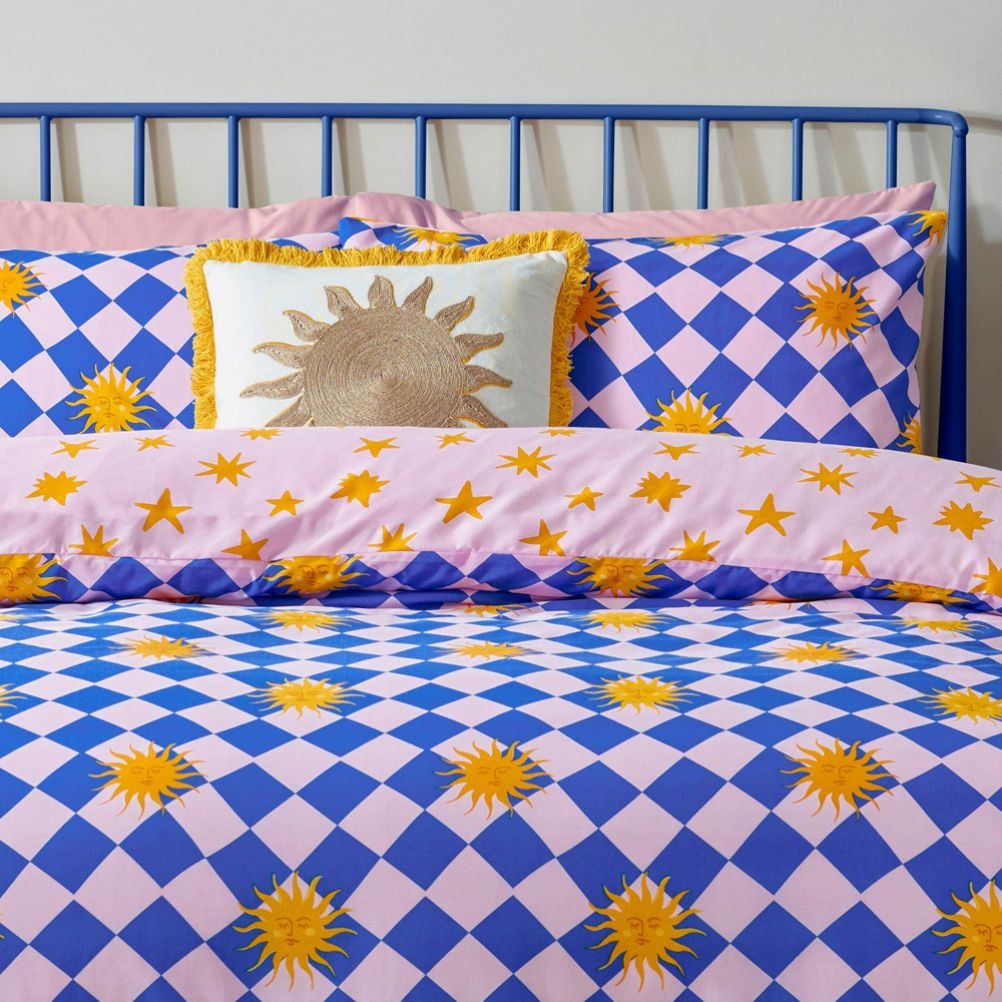 Colourful bedding with sun and star patterns, blue metal bed frame, and a decorative sun cushion. 