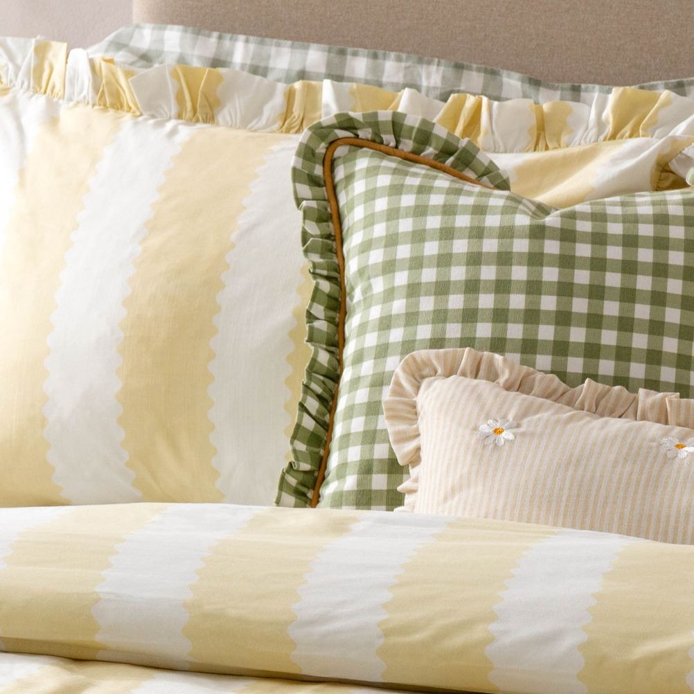 Three decorative pillows with yellow stripes and green gingham patterns on a bed. 