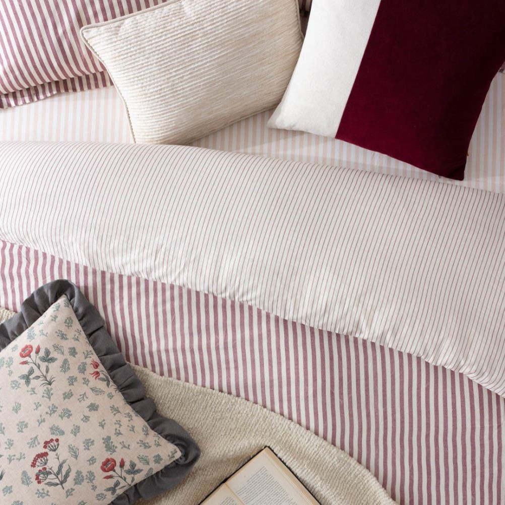 A bed with striped bedding, decorative pillows, and an open book. 