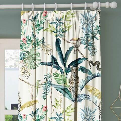 A printed curtain panel with a multicoloured jungle leopard design, hung on a white curtain pole in front of a muted green wall.