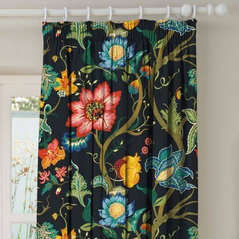 A black velvet curtain panel with a multicoloured printed floral design, hung on a white curtain pole in front of a neutral background.