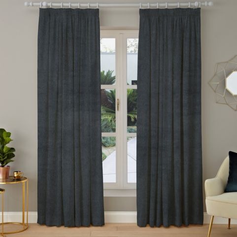 A pair of soft velvet curtains with a plain dye charcoal design, hung on a white curtain pole in front of a neutral background.