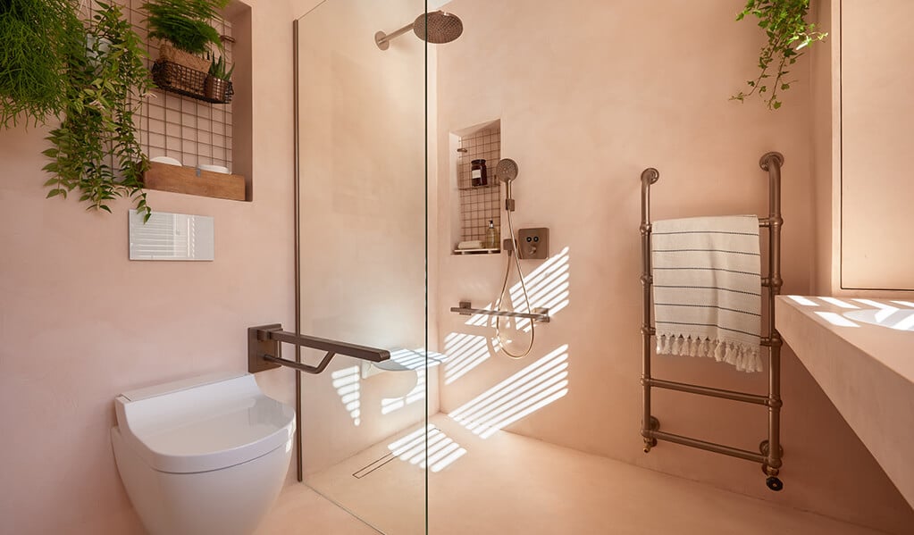 Ade and Linda's blush pink home bathroom, showing the stunning finish of a modern Doc M pack, integrated plantation adding a splash of colour. 
