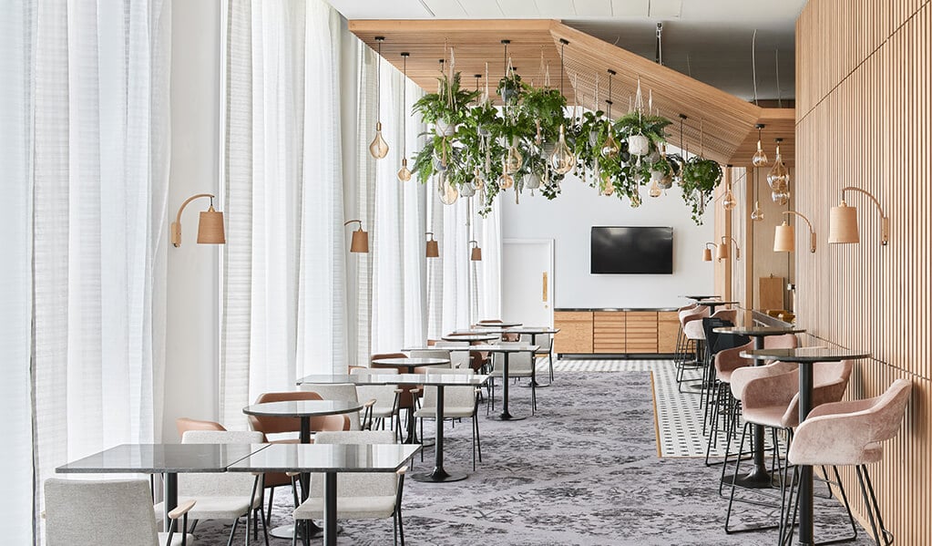 Hotel Brooklyn dining area, beautiful vertical light wood panelling running across the ceiling as well as adjacent to the floor to ceiling windows. Complimented with light wood wall lights and ceiling hung plantation with exposed bulbs. 
