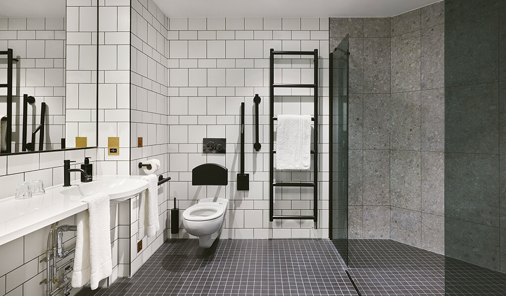 Hotel Brooklyn accessible shower, toilet and basin featuring matt black finishes throughout contrasting with white metro tiles. 