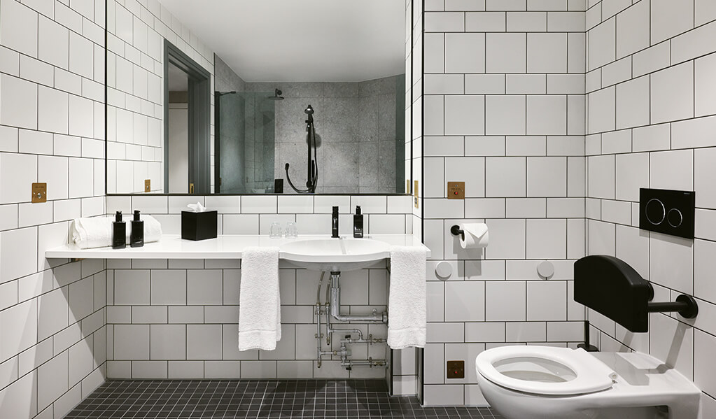Hotel Brooklyn accessible basin and toilet featuring matt black finishes throughout contrasting with white metro tiles. 
