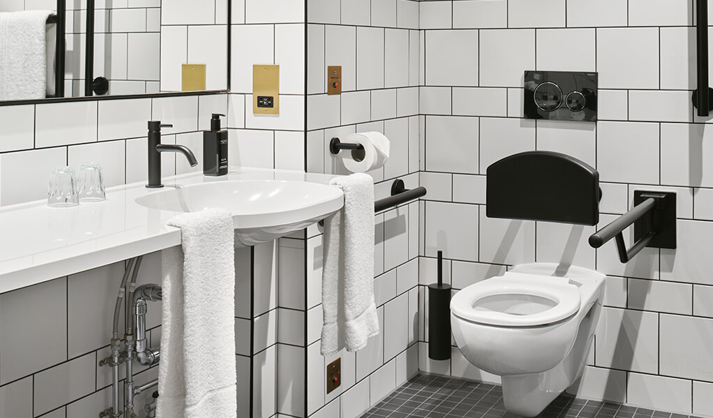 Hotel Brooklyn white tiled, black tile trim bathroom, showcasing the wall hung toilet with matt black back rest.
