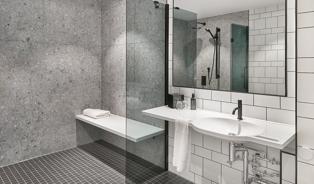 Hotel Brooklyn bathroom showcasing a sleek shower bench and glass shower door. 
