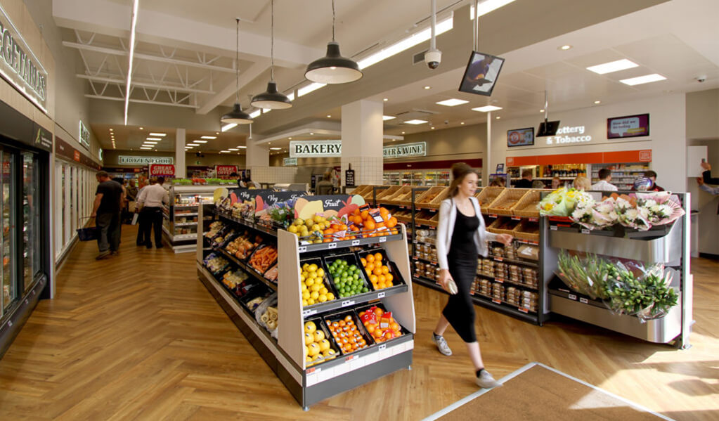 Interior of the Budgens store, displaying the light herringbone wood floor, colourful fruit and vegetables and bakery. 
