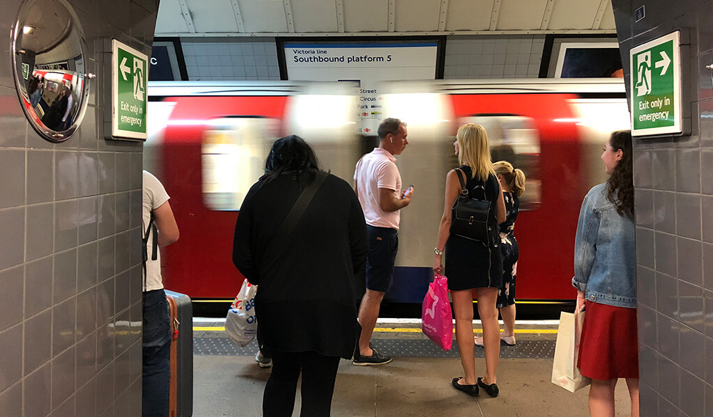 London underground tube station of a moving tube with individuals. 
