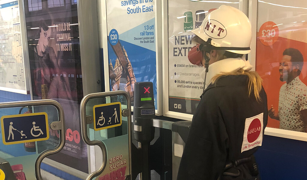 Person in an M.I.T age lab suit going through accessible ticket gates at train station
