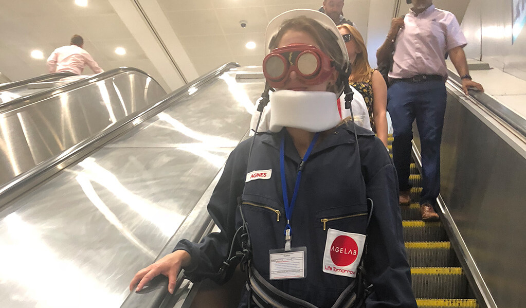 Person in a M.I.T age lab suit travelling down an underground escalator during a busy commute
