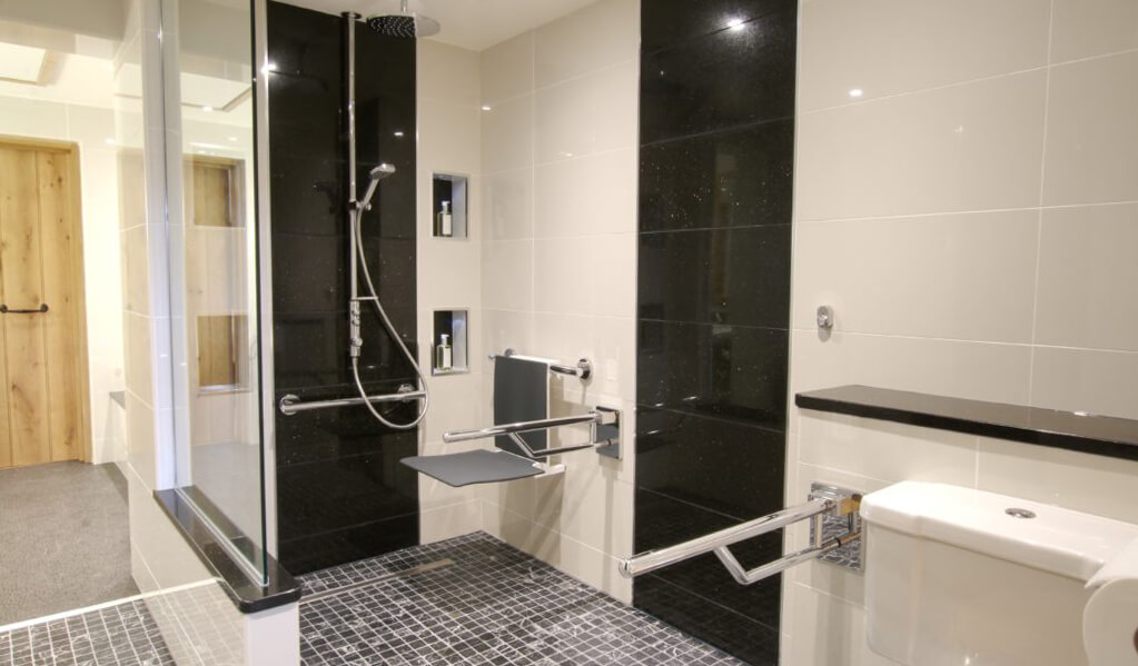 Monochrome interior tiled bathroom with view of chrome shower and charcoal grey seat down.
