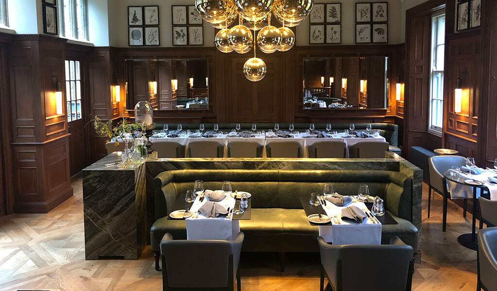 Dark wood panelled dining room with olive green upholstery and statement gold globe ceiling lap
