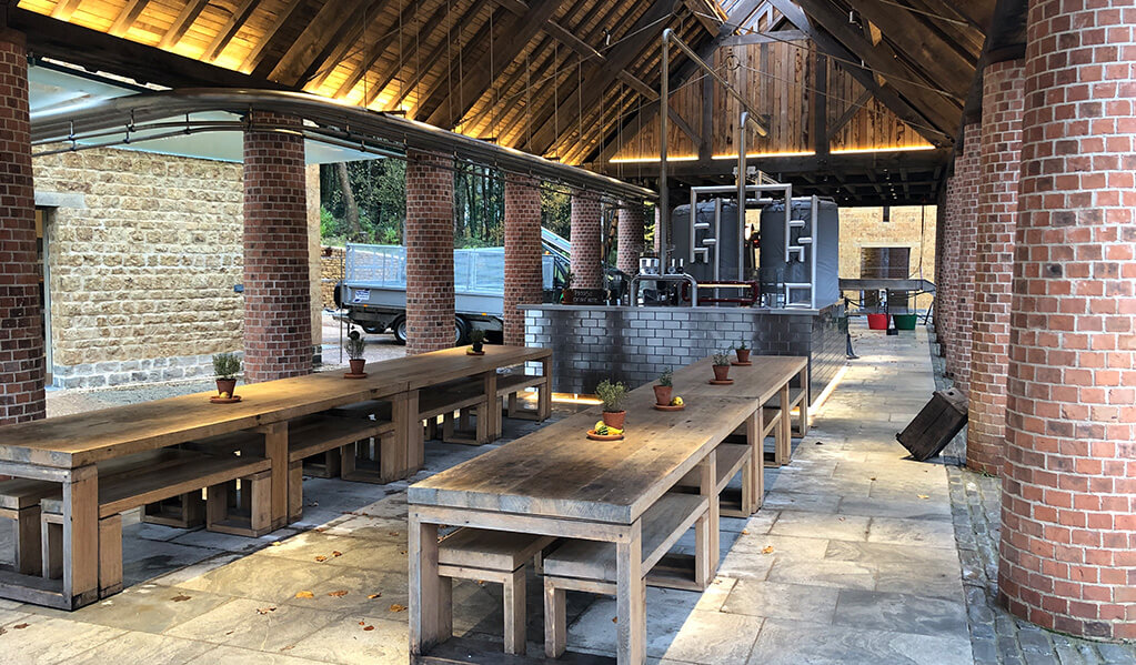 Open sided barn with brick columns and long wooden dining table down the central aisle
