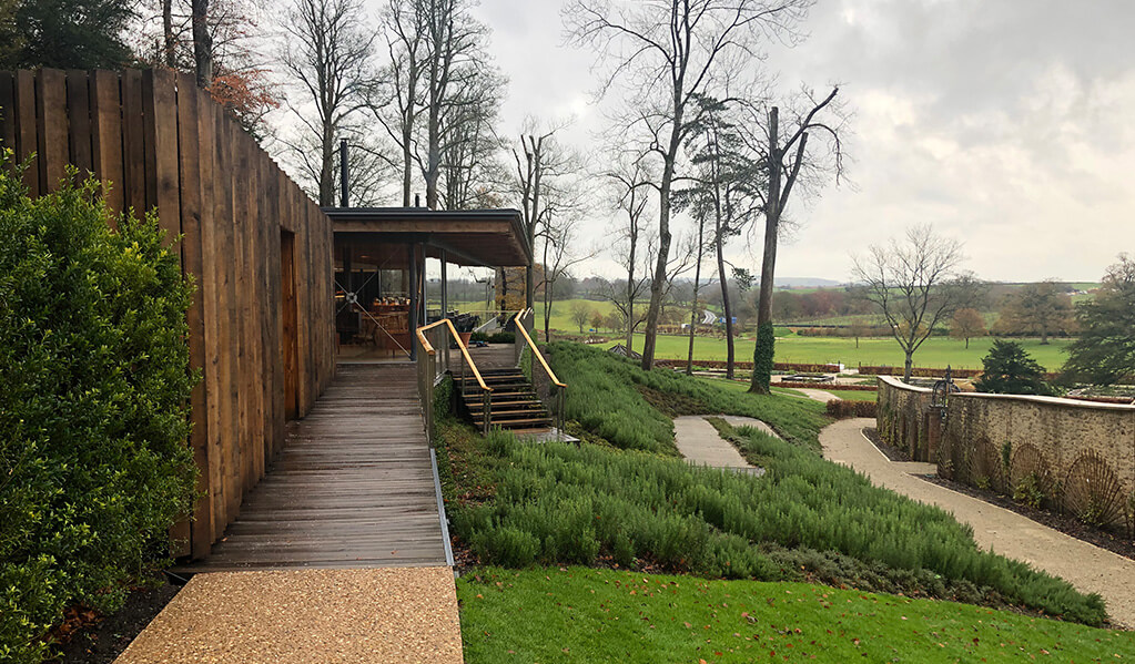 Wooden exterior of a dining area over looking gardens with stairs and ramps built into greenery
