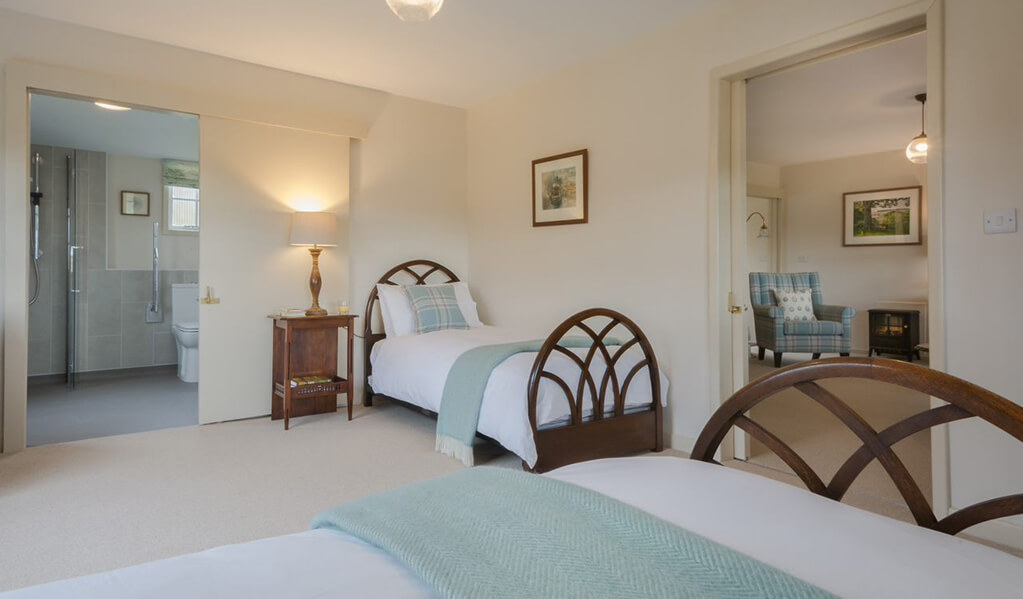 Cream coloured bedroom with two single chocolate brown beds, lovely teal blue soft furnishings leading into the lounge area. 
