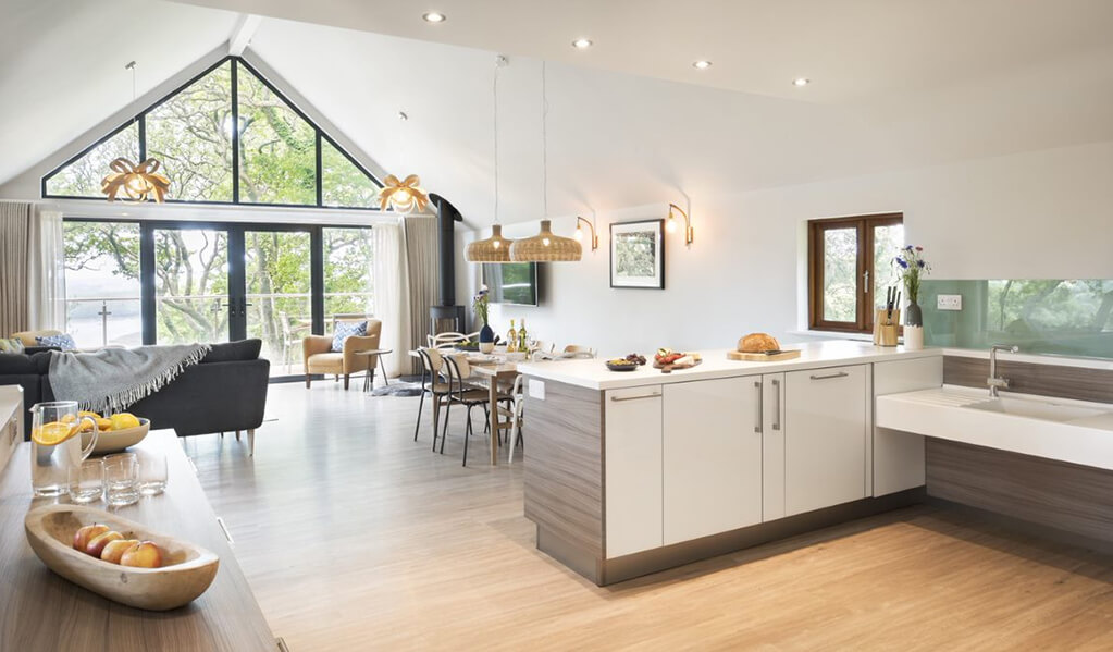 Open plan view of high ceiling living area from kitchen. Beautiful mustard finishes throughout with light wood flooring and clean white painted walls.  
