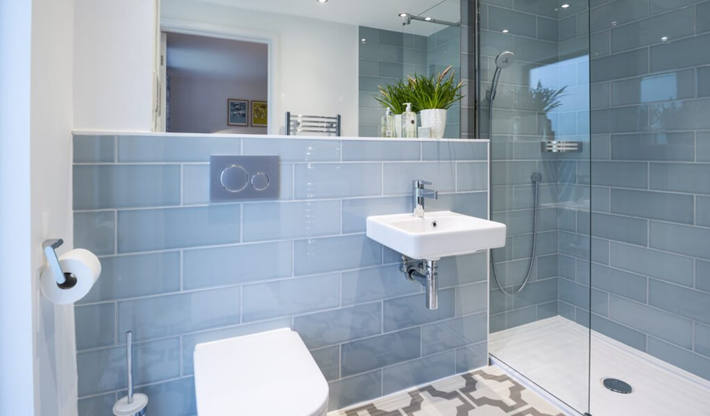 Details of large rectangle light blue wall tiles in bathroom with patterned grey and white flooring. 
