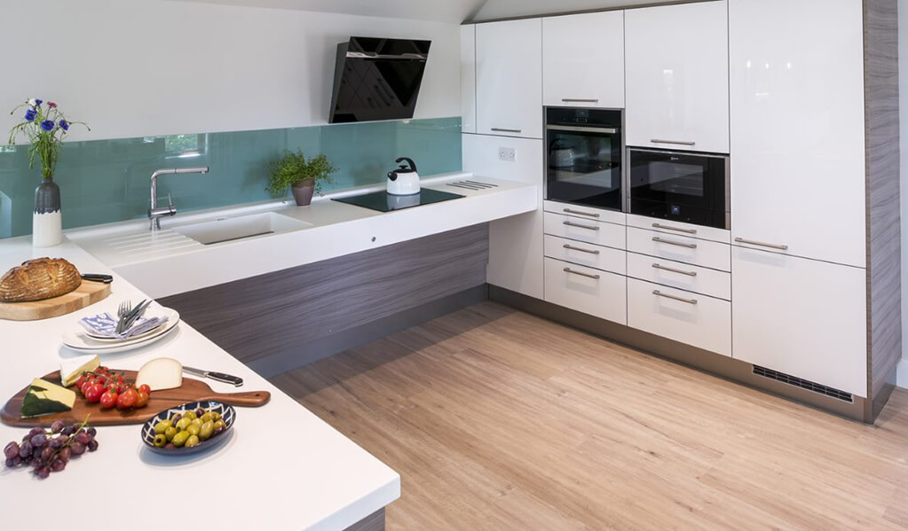 Grey wood and white U shaped smart modern kitchen with light wood flooring and chrome finishes. 
