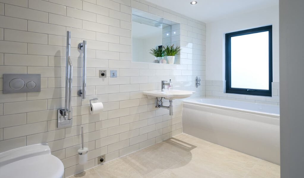 White modern tiled accessible bathroom with chrome finishes and a large white bath. 
