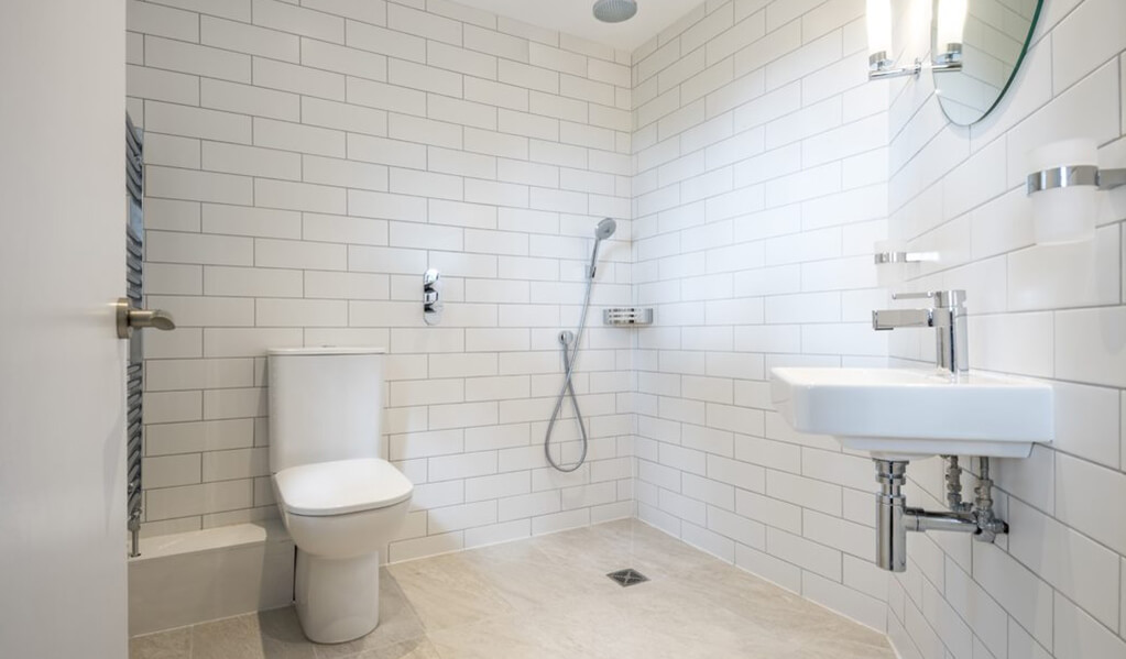 White modern tiled shower room with chrome finishes and standing toilet. 
