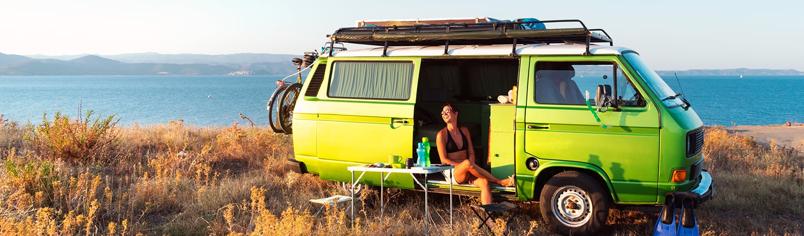 Female sitting in a green campervan near the ocean