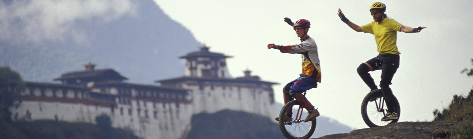 Two unicyclists riding down a hill