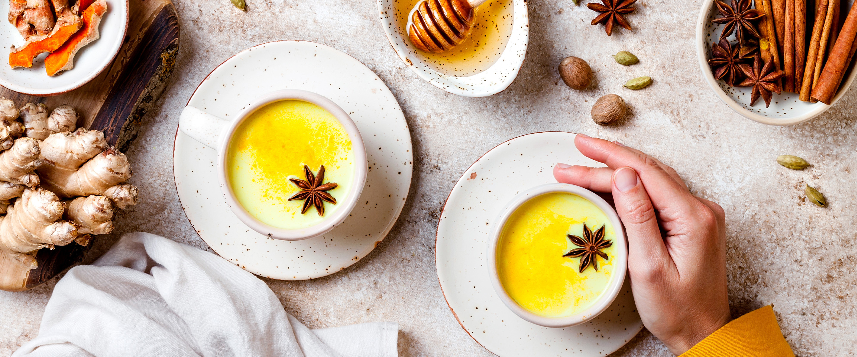Cups of turmeric tea with saucers, spices and white napkins