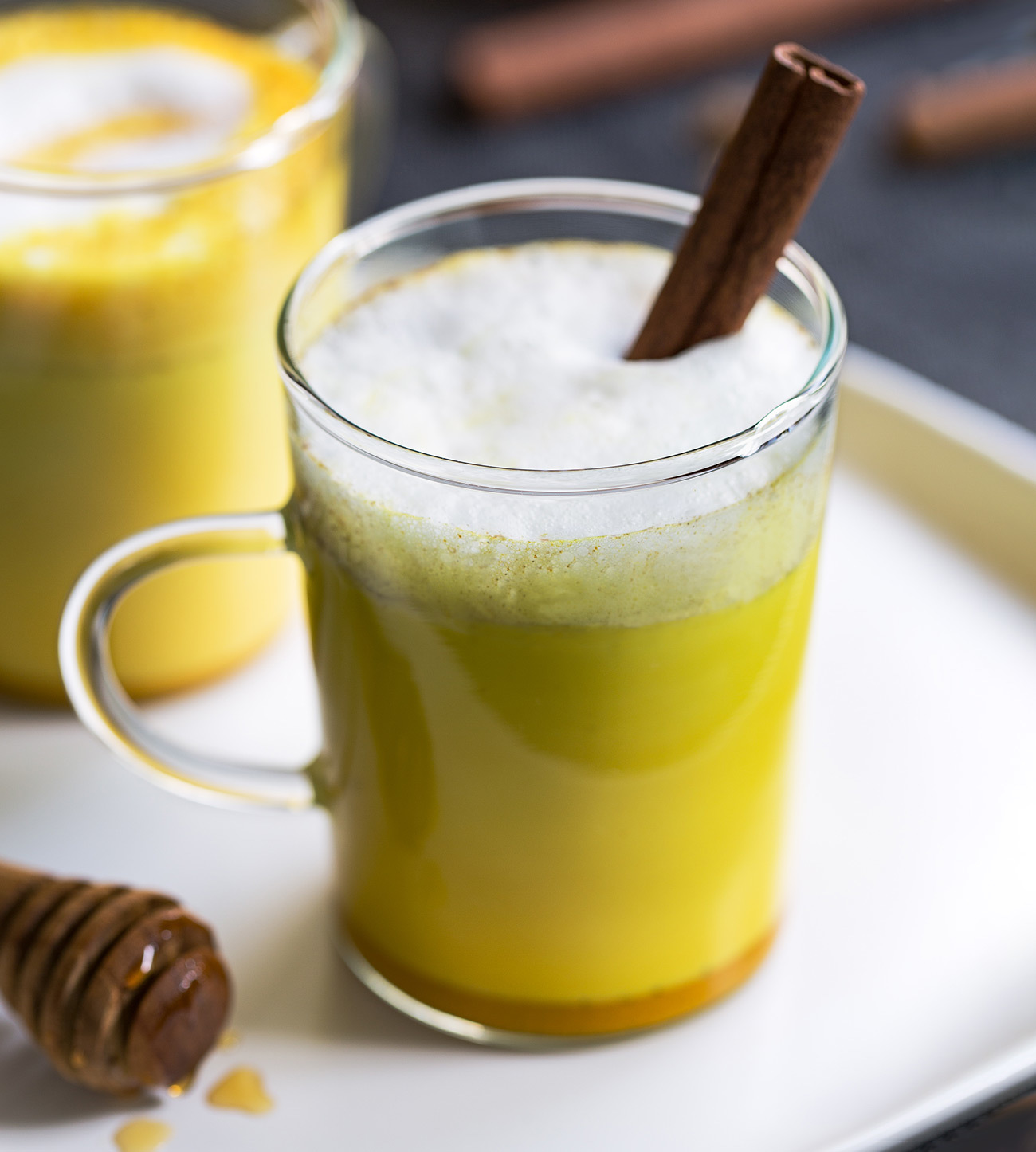 Glass cup of golden milk garnished with a cinnamon stick