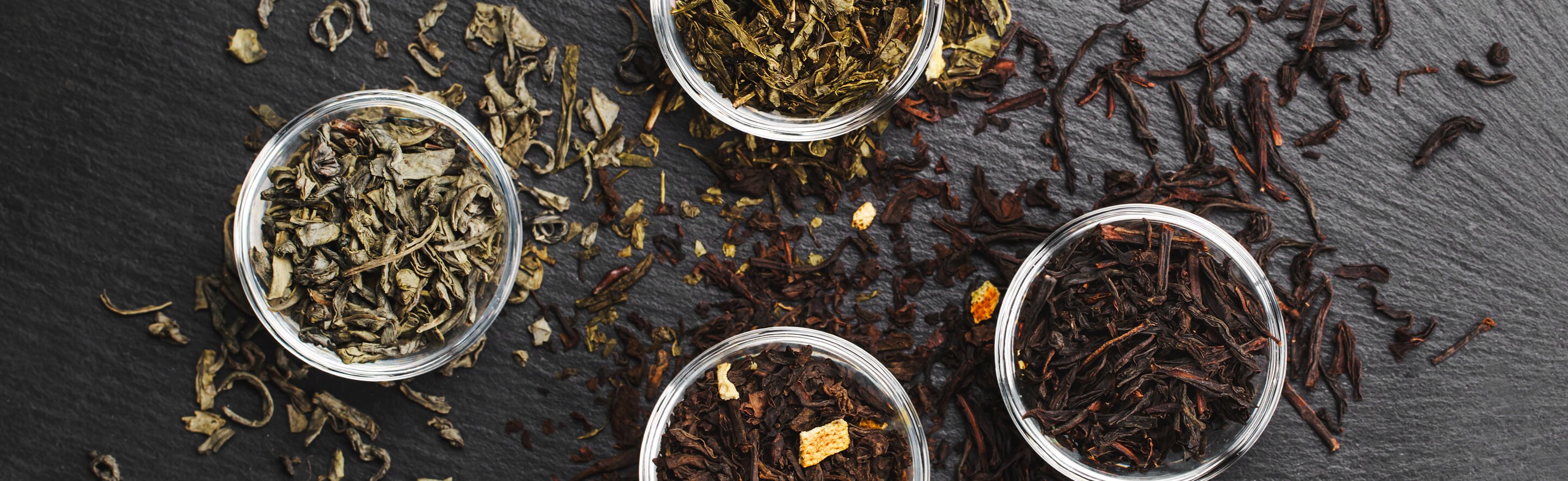 Bowls of loose tea on a dark table with tea spilled out on the table