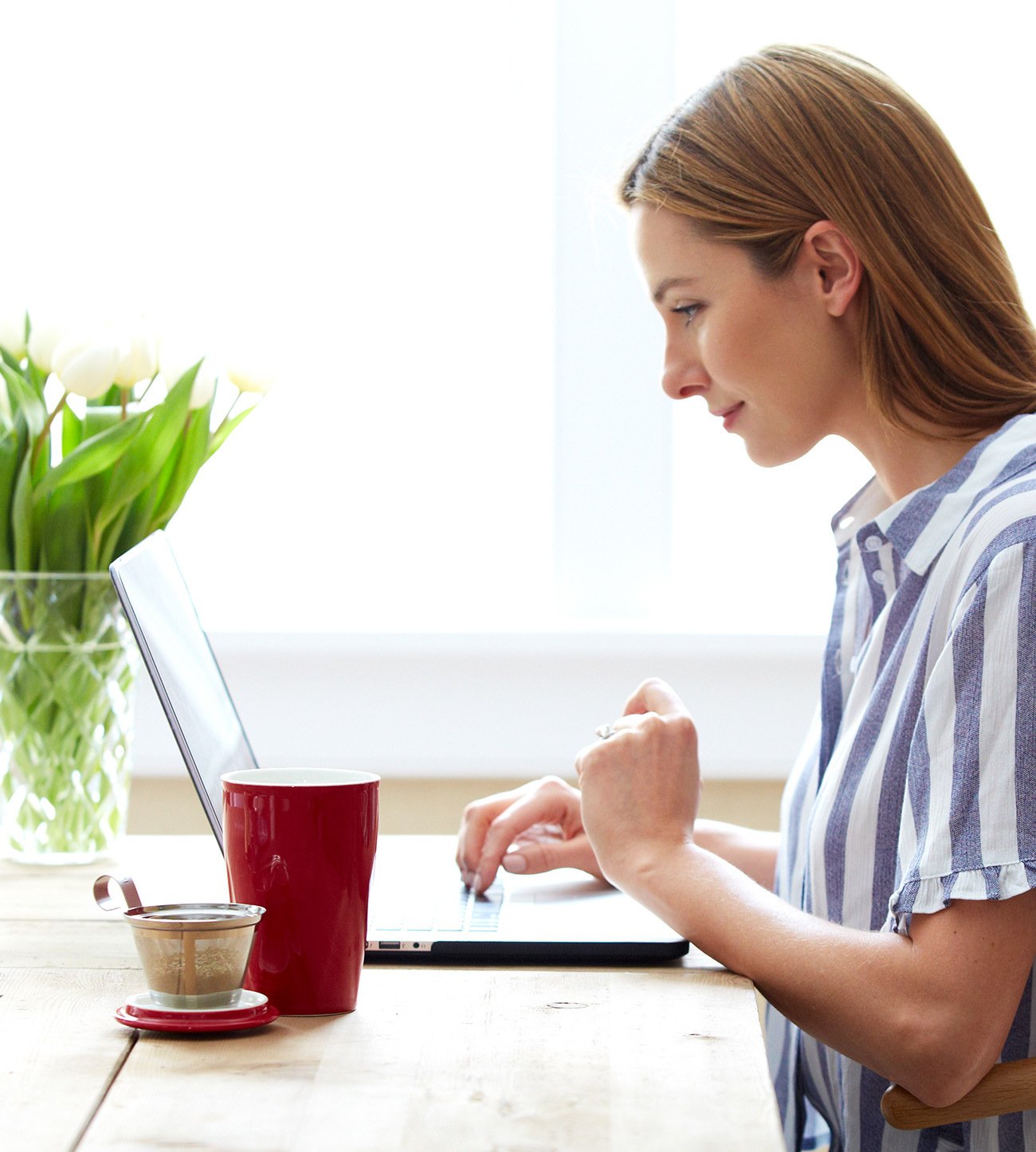 Woman working at a laptop at a sunny desk with a KATI Steeping Cup on the table