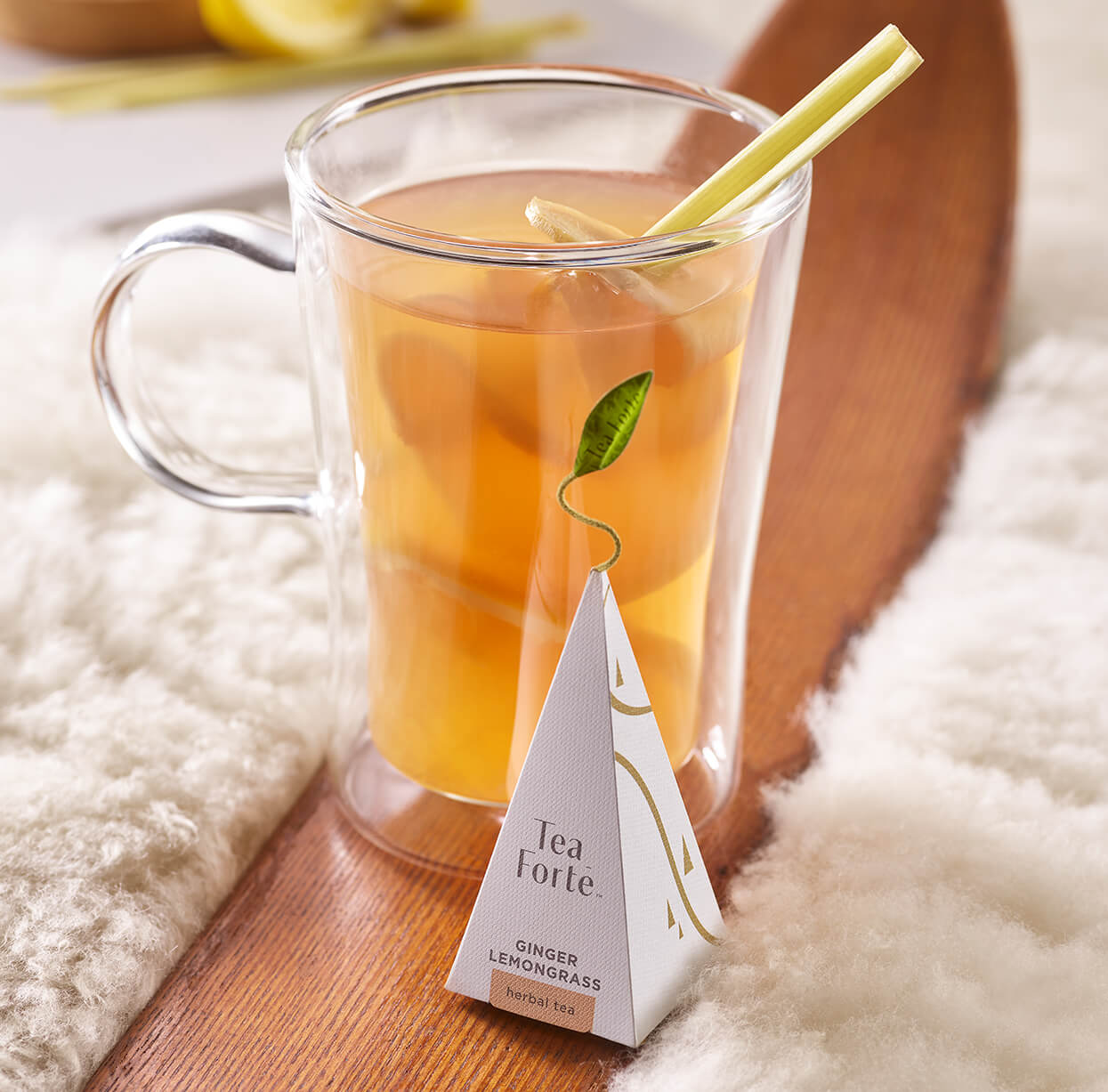 Ginger lemongrass hot toddy in a glass mug on a wooden ski on a white furry blanket with a pyramid infuser