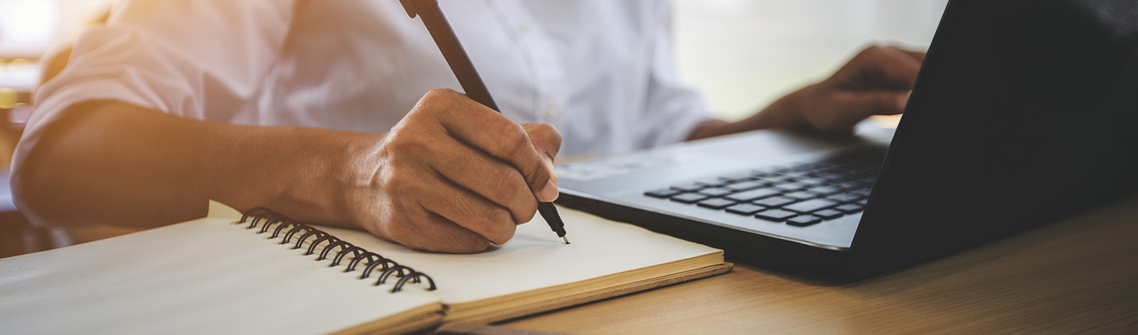 Woman taking notes while learning online with laptop