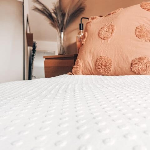 A white 100% cotton duvet cover set with a tufted polka dot design, made on a bed with a pink tufted pillow sham.