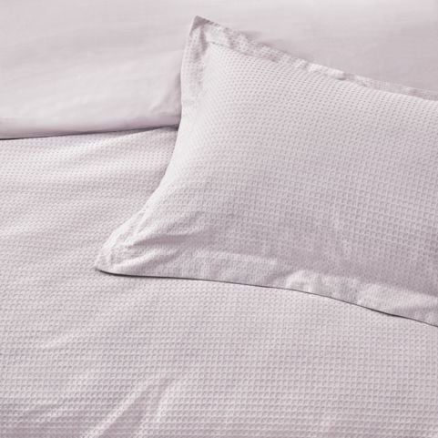 A closeup image of a waffle textured cotton duvet set in a light blush pink shade.